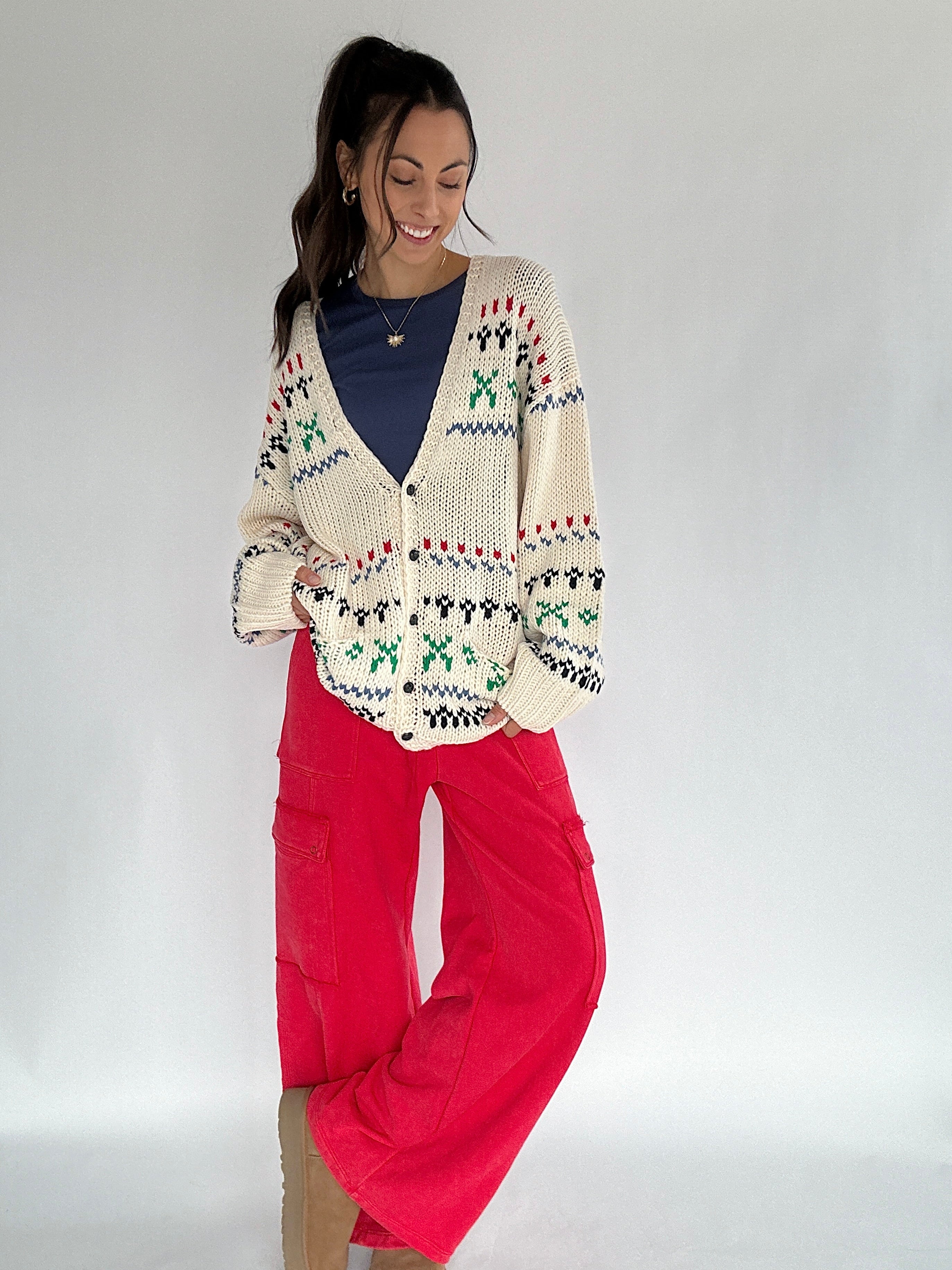 Woman wearing a patterned cardigan and red pants on a plain background