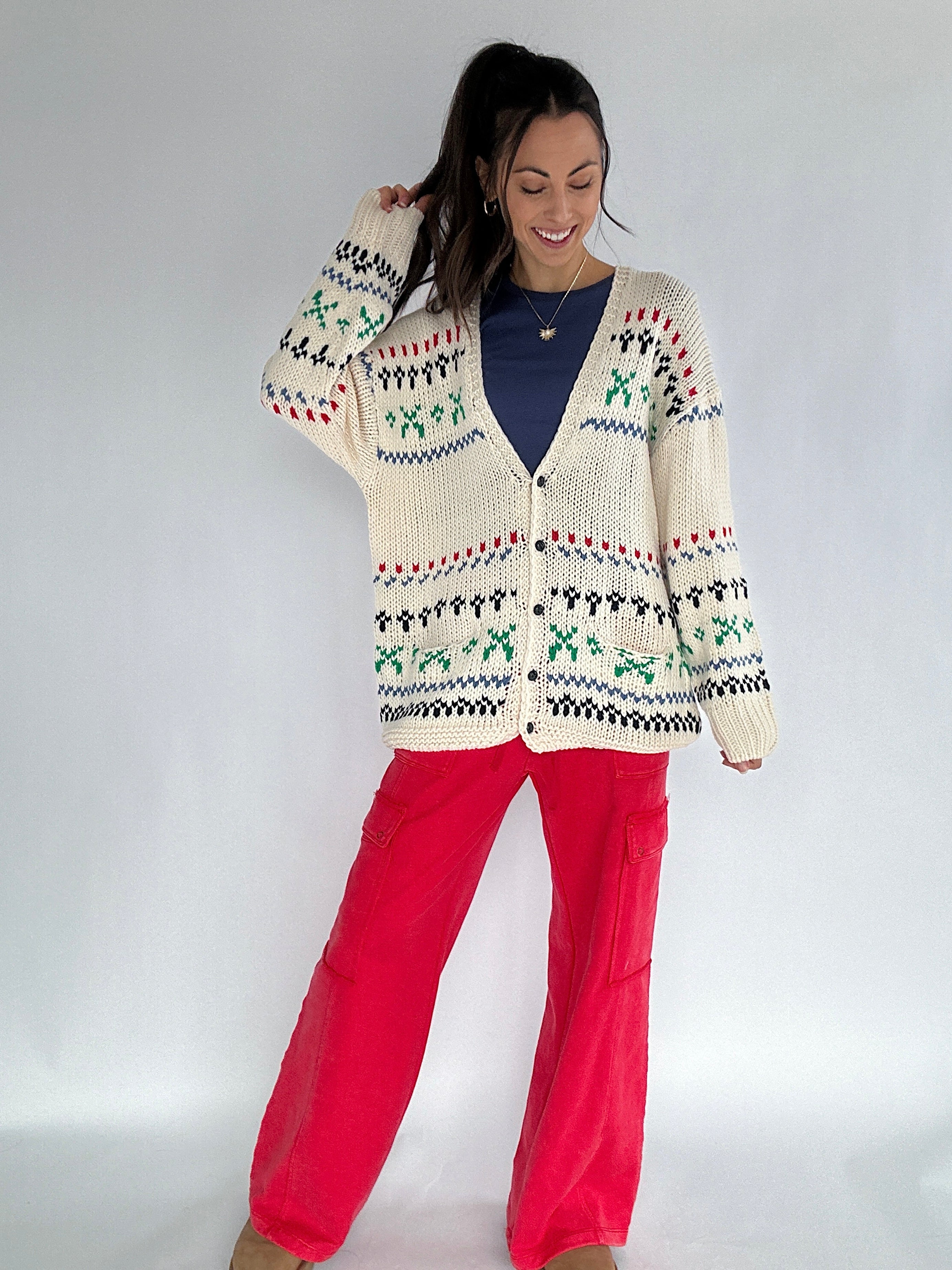 Woman wearing a patterned cardigan and red pants against a white background