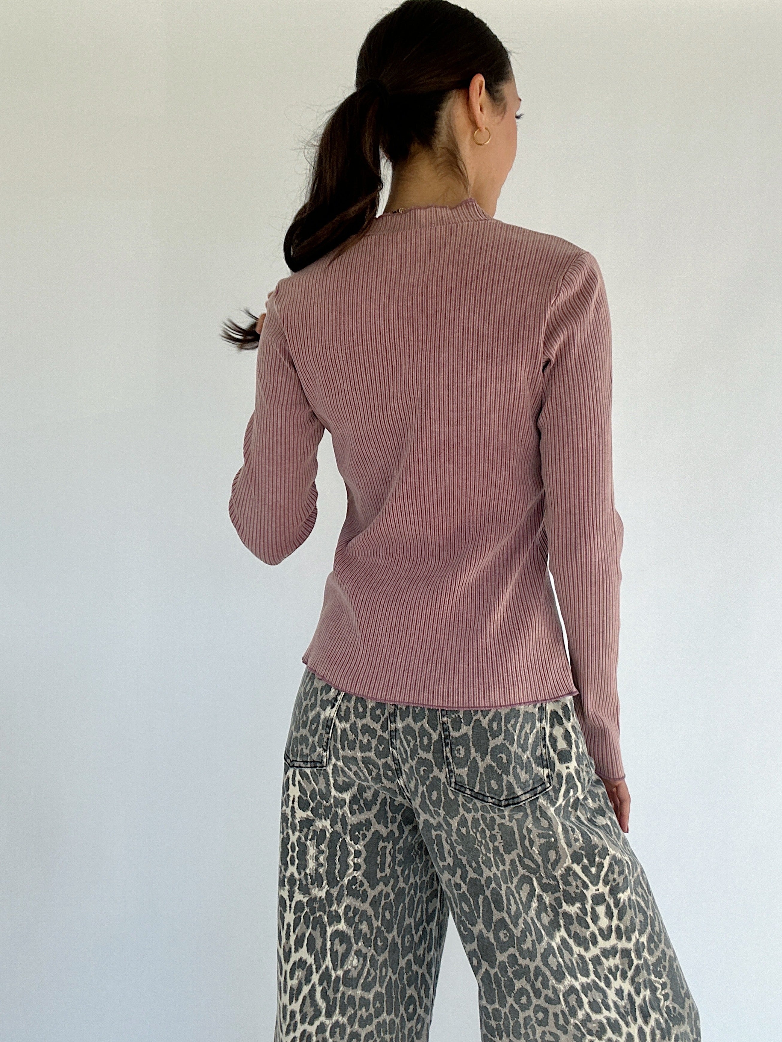 Person wearing a pink ribbed sweater and leopard print pants against a white background