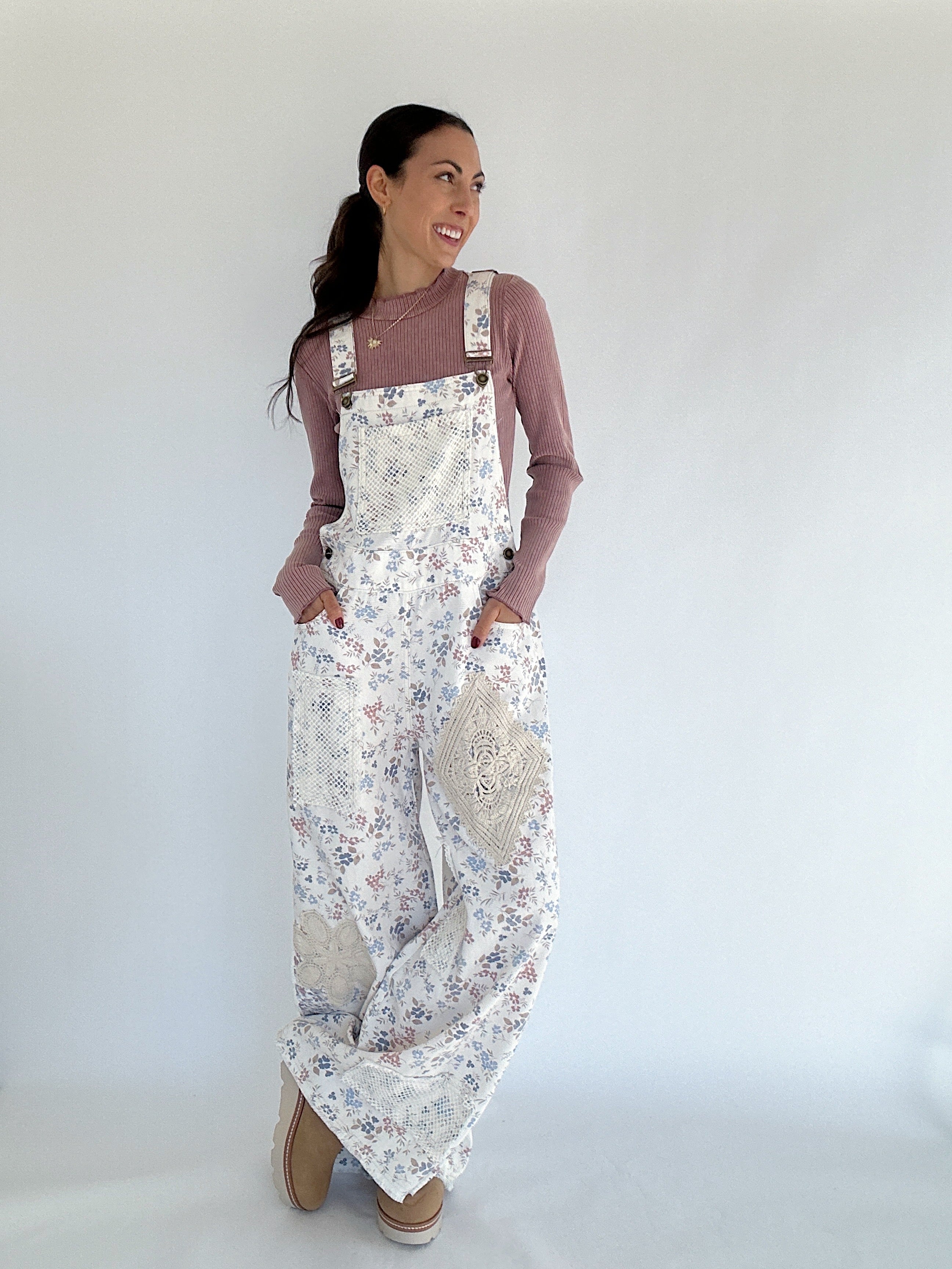 Woman wearing floral overalls with long sleeve top against a white background