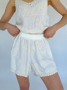 Person wearing a white lace top and shorts set against a plain background