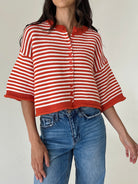 A woman wearing a cropped, short-sleeve knit cardigan with red and white horizontal stripes, paired with blue jeans, against a plain light background.