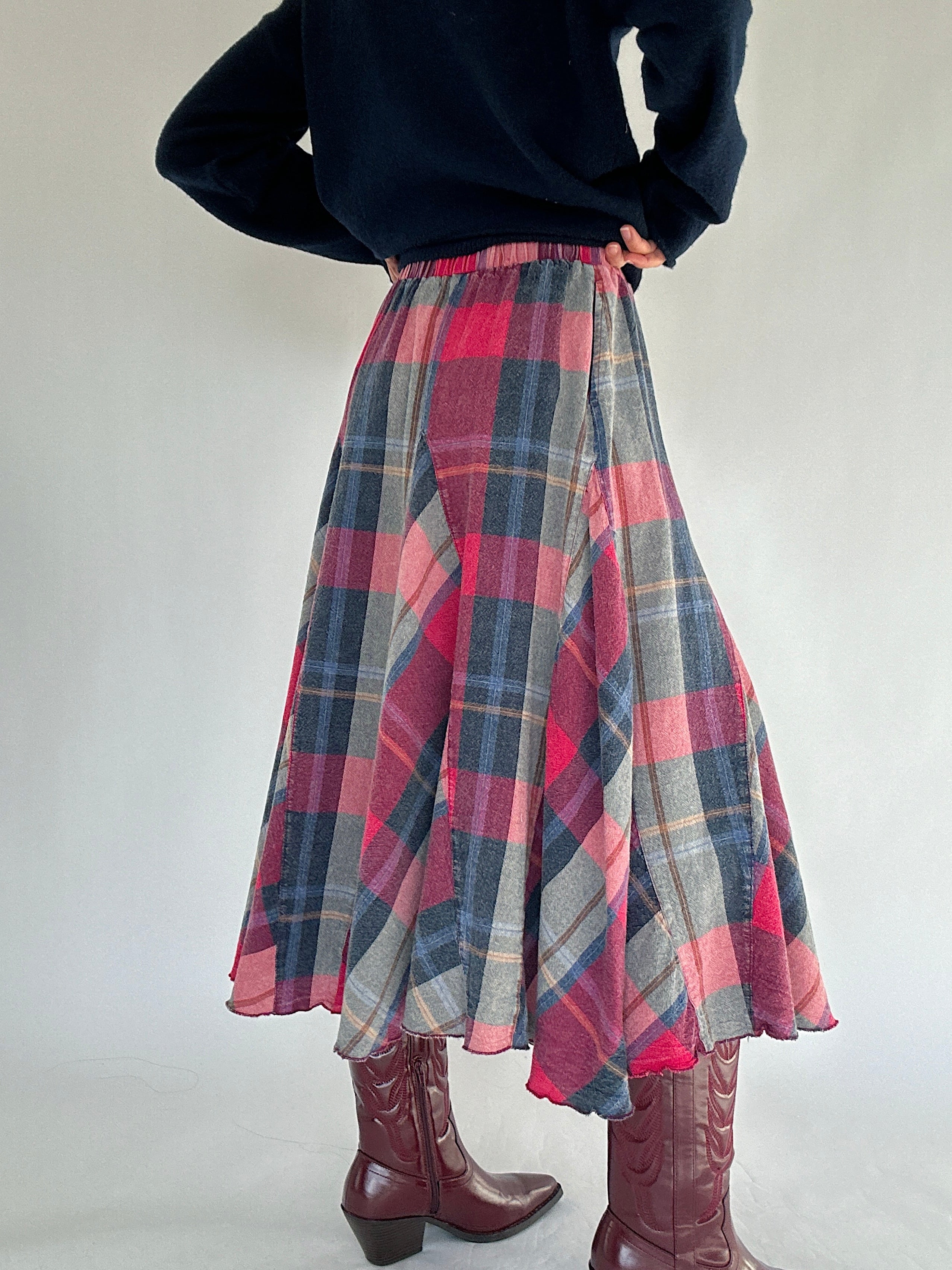Person wearing a plaid skirt and dark sweater on a plain background from back