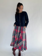 Woman wearing a navy cardigan sweater and plaid skirt on a white background