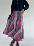 Person wearing a navy sweater and plaid skirt on a white background