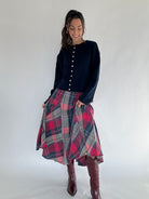 Woman wearing a navy cardigan top and plaid skirt with burgundy boots on a white background