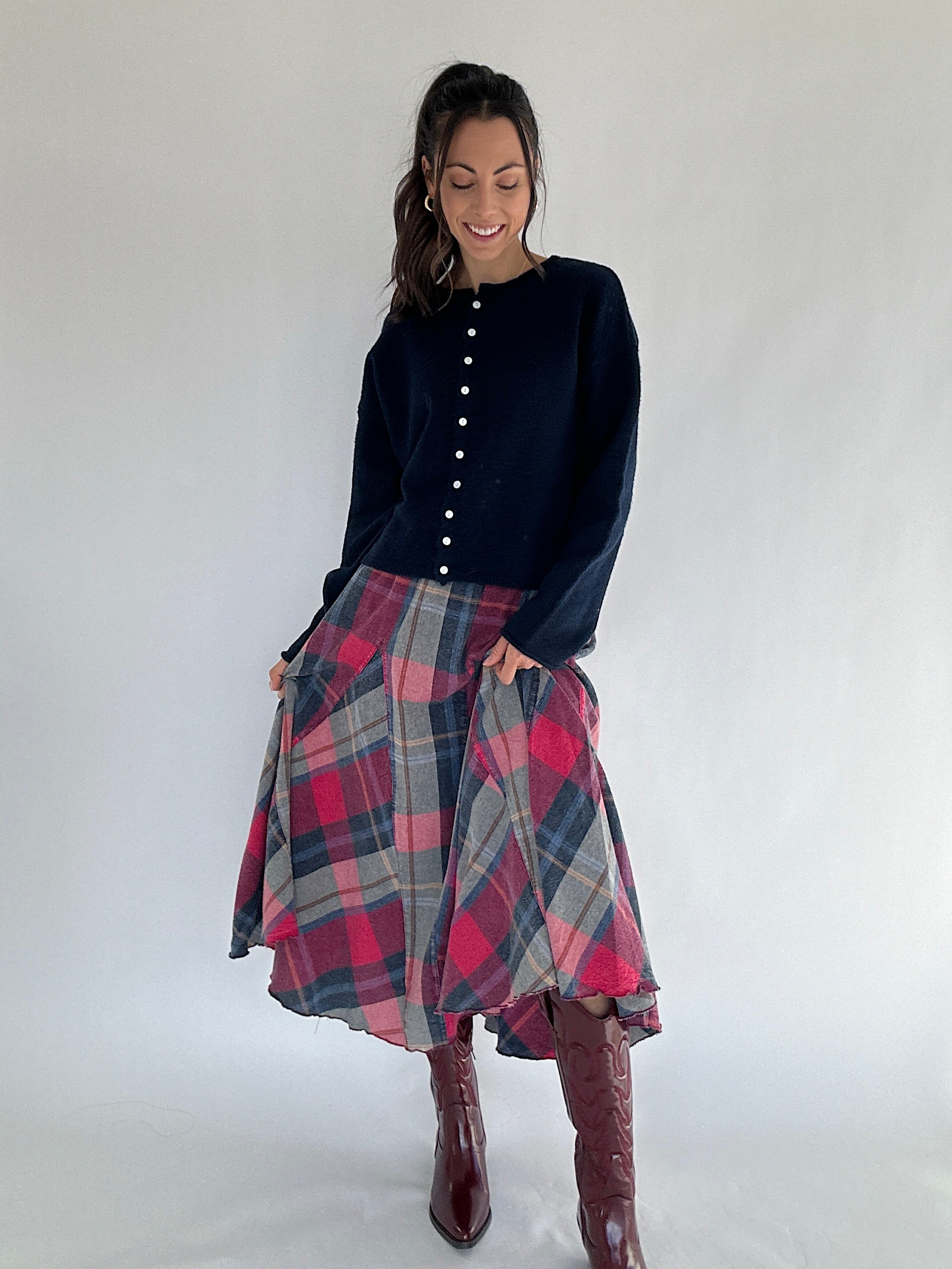 Woman wearing a navy cardigan top and plaid skirt with burgundy boots on a white background