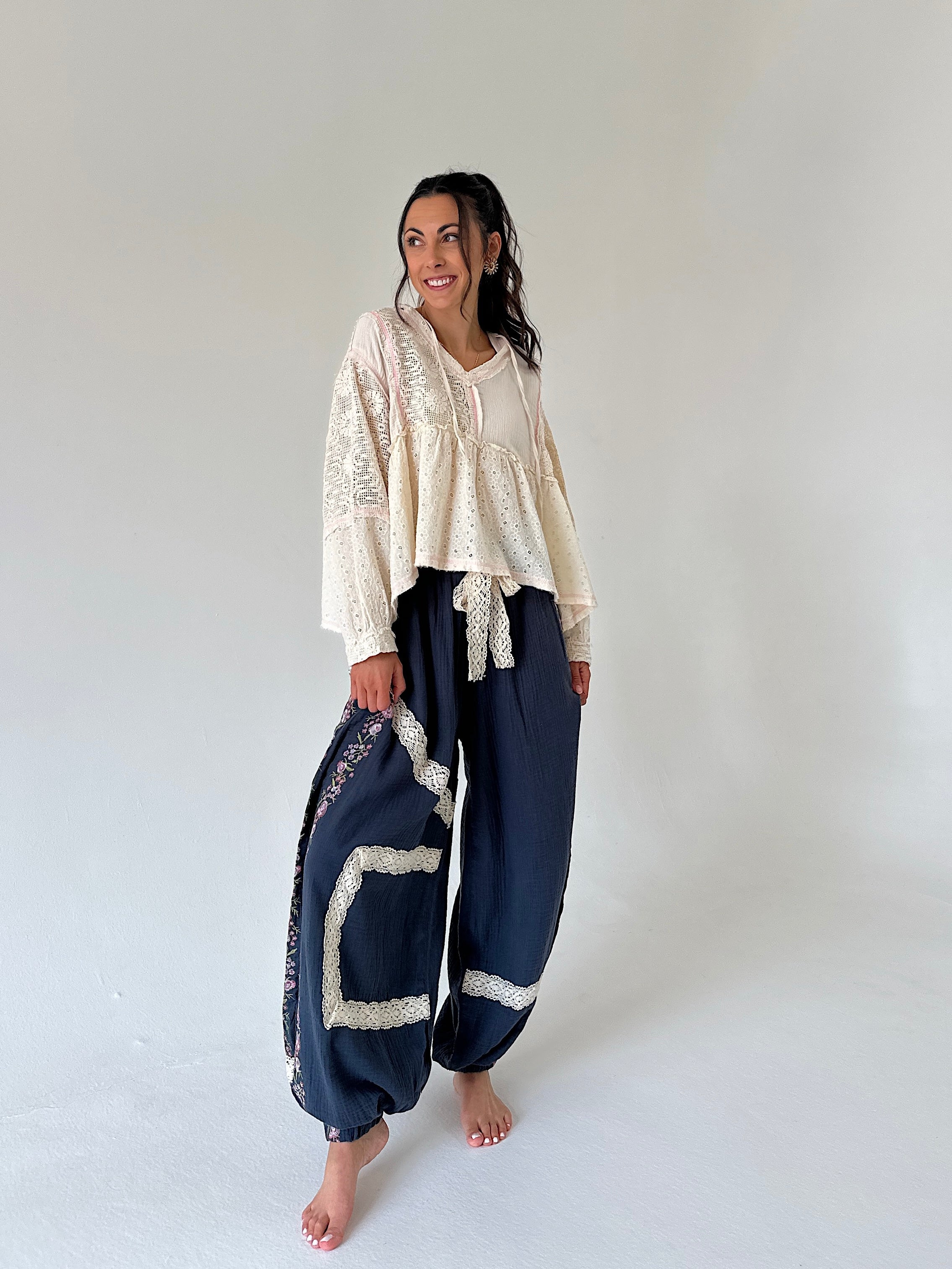 A woman modeling a bohemian-style outfit consisting of a cream lace-trimmed long-sleeve top and navy blue harem pants with cream lace trim, standing against a plain white studio background.