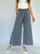 Person wearing gray wide-leg sweatpants and white tee and metallic sneakers on a plain background