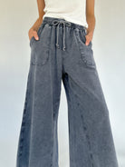 Person wearing wide-leg sweatpants with a white top on a light background showing drawstring waistband and pockets