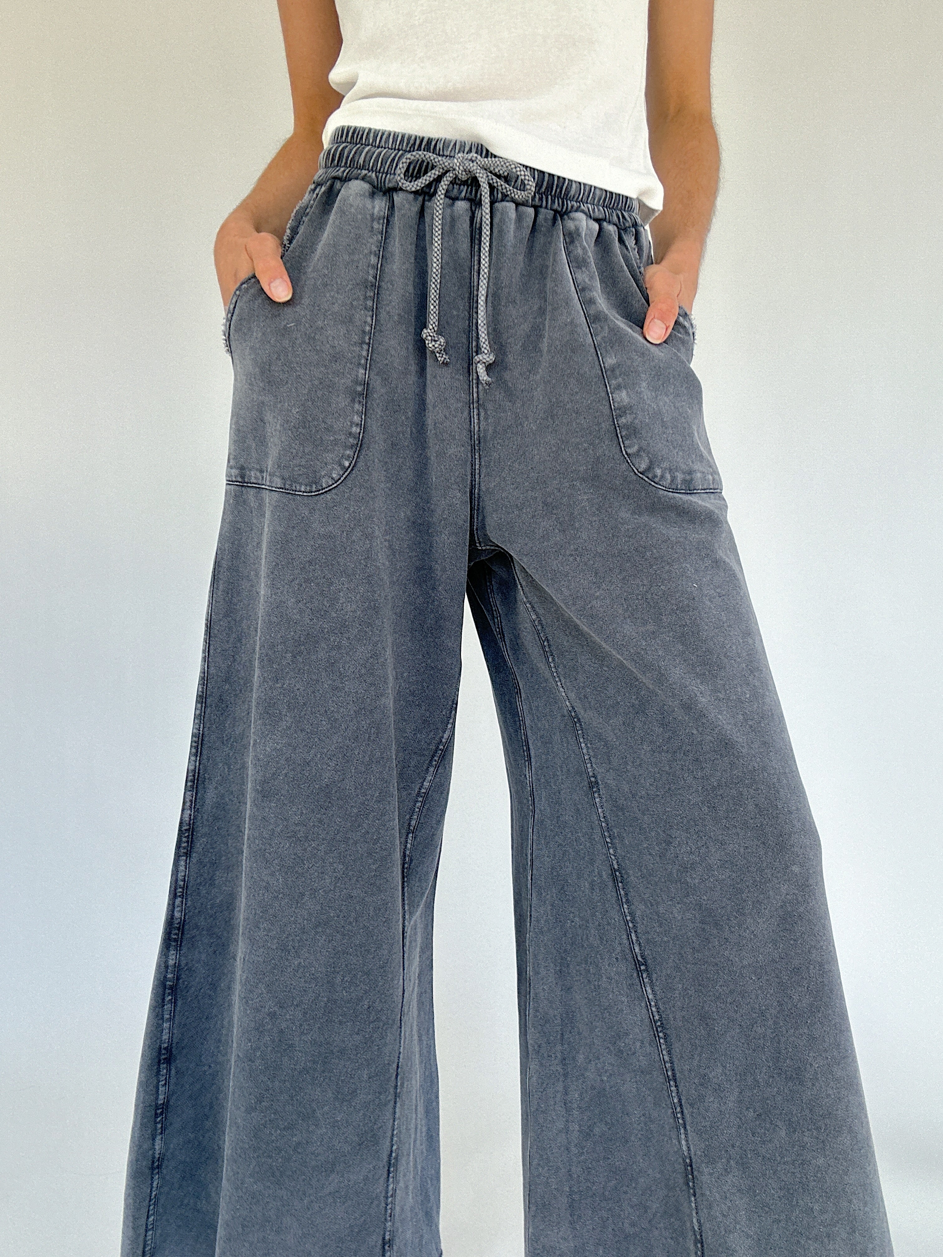 Person wearing wide-leg sweatpants with a white top on a light background showing drawstring waistband and pockets