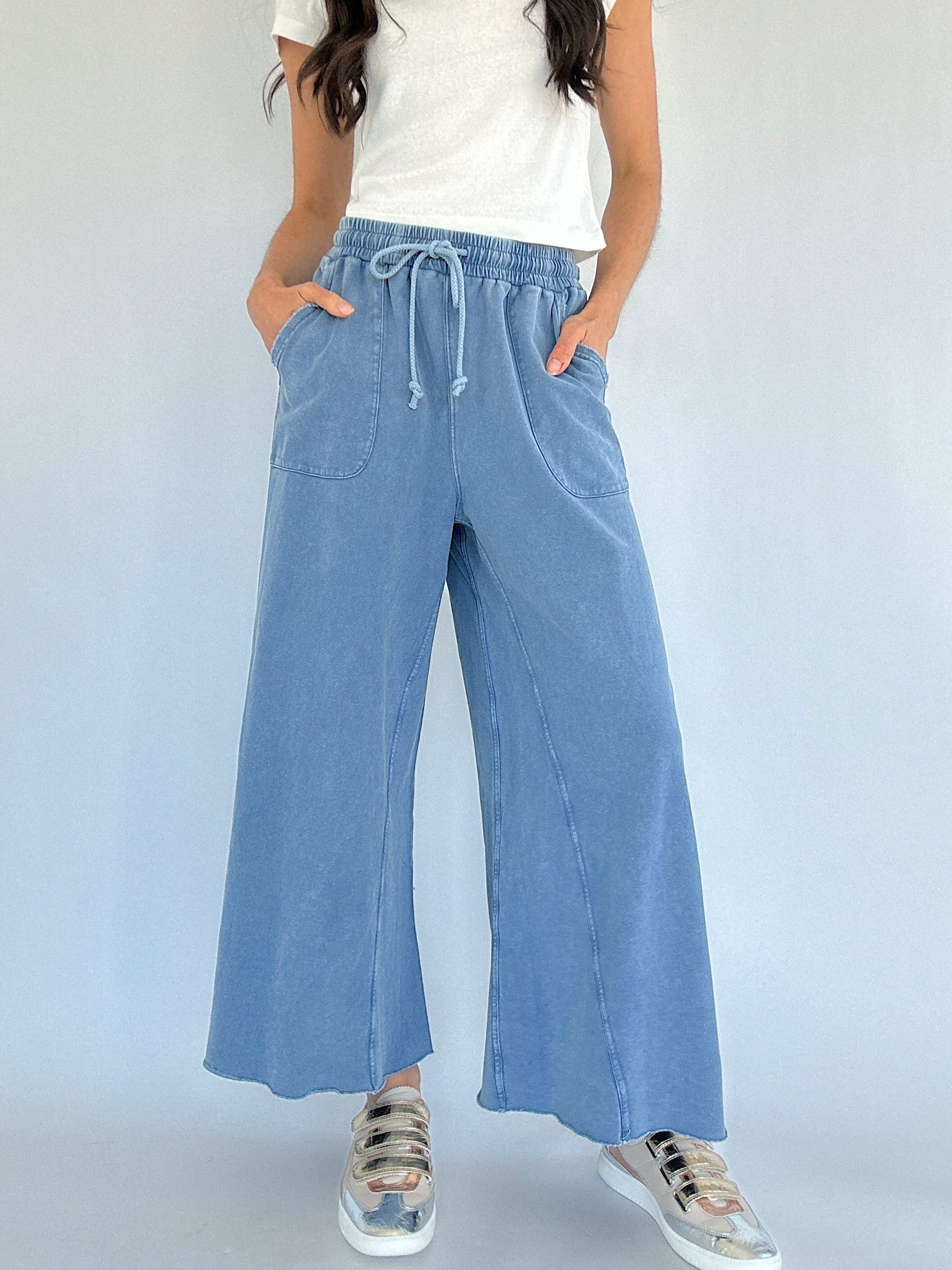 Person wearing light blue wide-leg sweatpants with a white top on a plain background