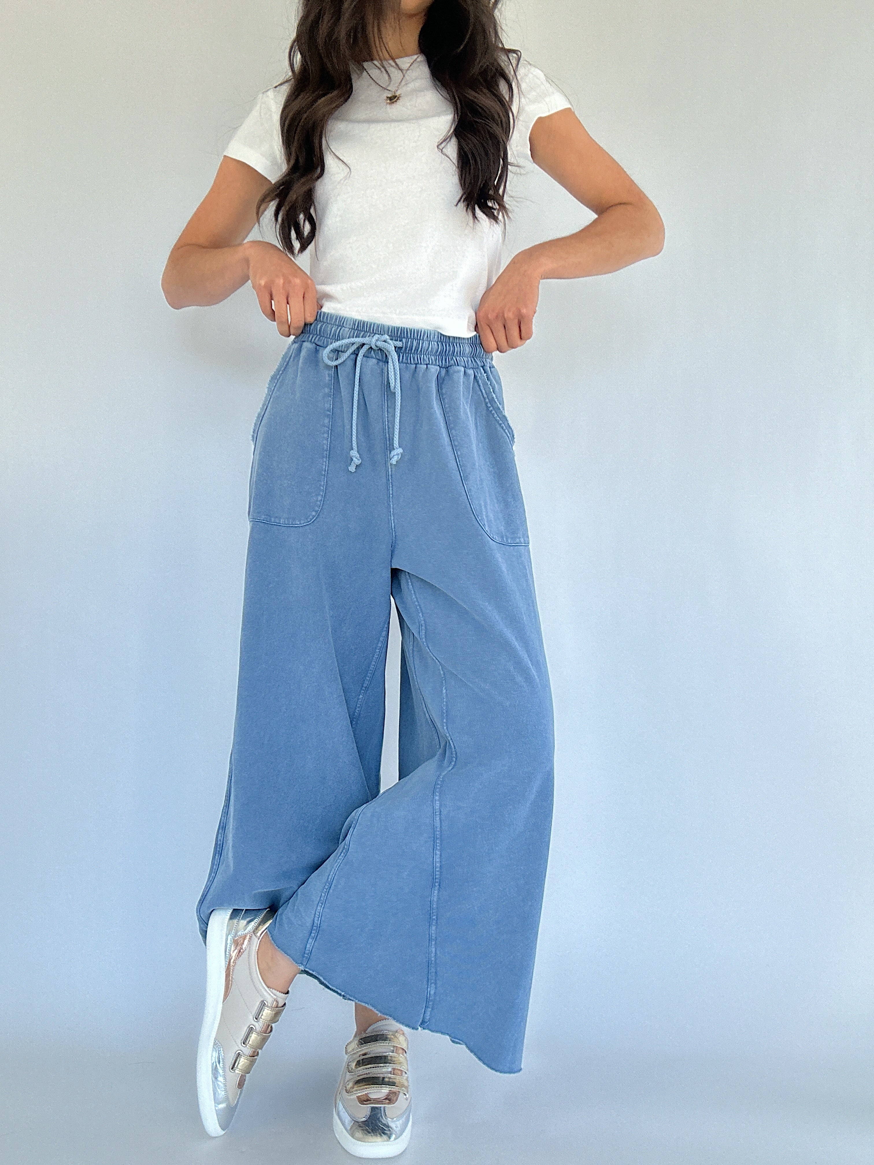 Person wearing a white top and blue wide-leg sweatpants against a plain background