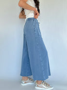 Person wearing light blue wide-leg sweatpants and metallic sneakers on a plain background showing side