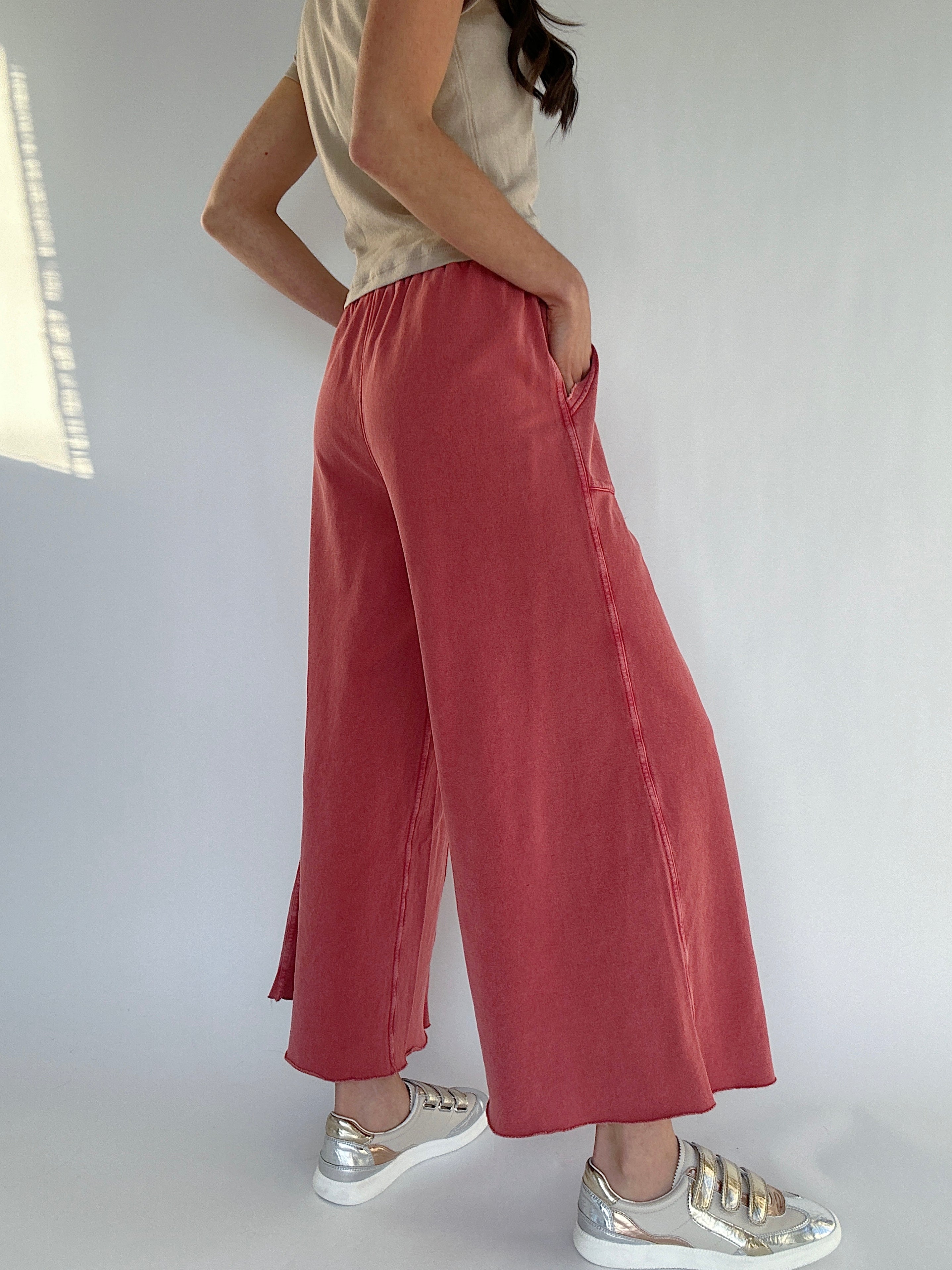 Person wearing red wide-leg sweatpants and silver sneakers on a white background showing backside