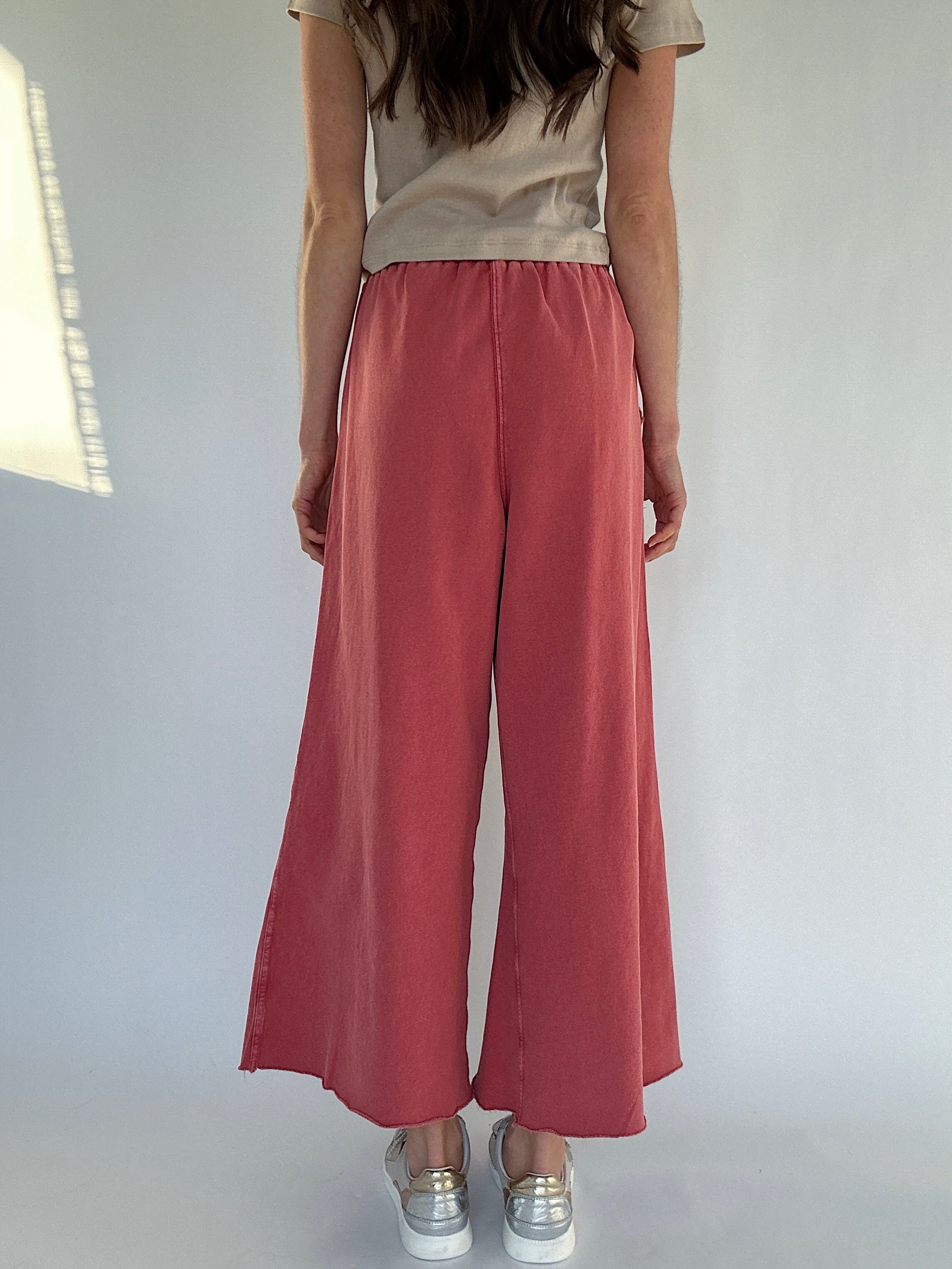 Person wearing a beige tee and red wide-leg pants against a plain background showing backside