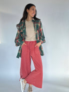 Woman wearing a green plaid shirt, beige tee, red sweatpants, and metallic sneakers on a plain background