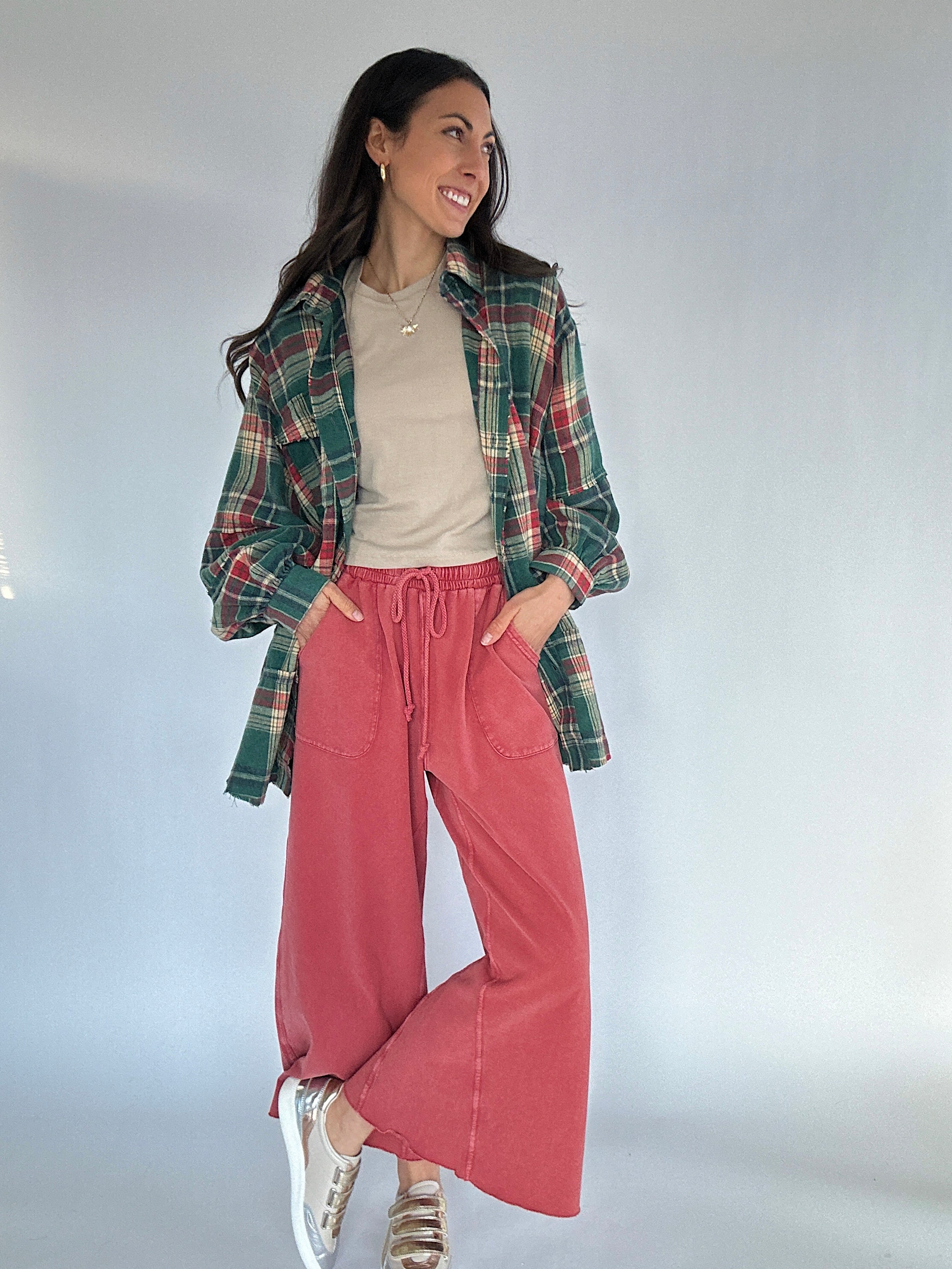 Woman wearing a green plaid shirt, beige tee, red sweatpants, and metallic sneakers on a plain background