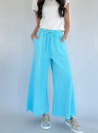Person wearing light blue wide-leg pants with a white top on a plain background
