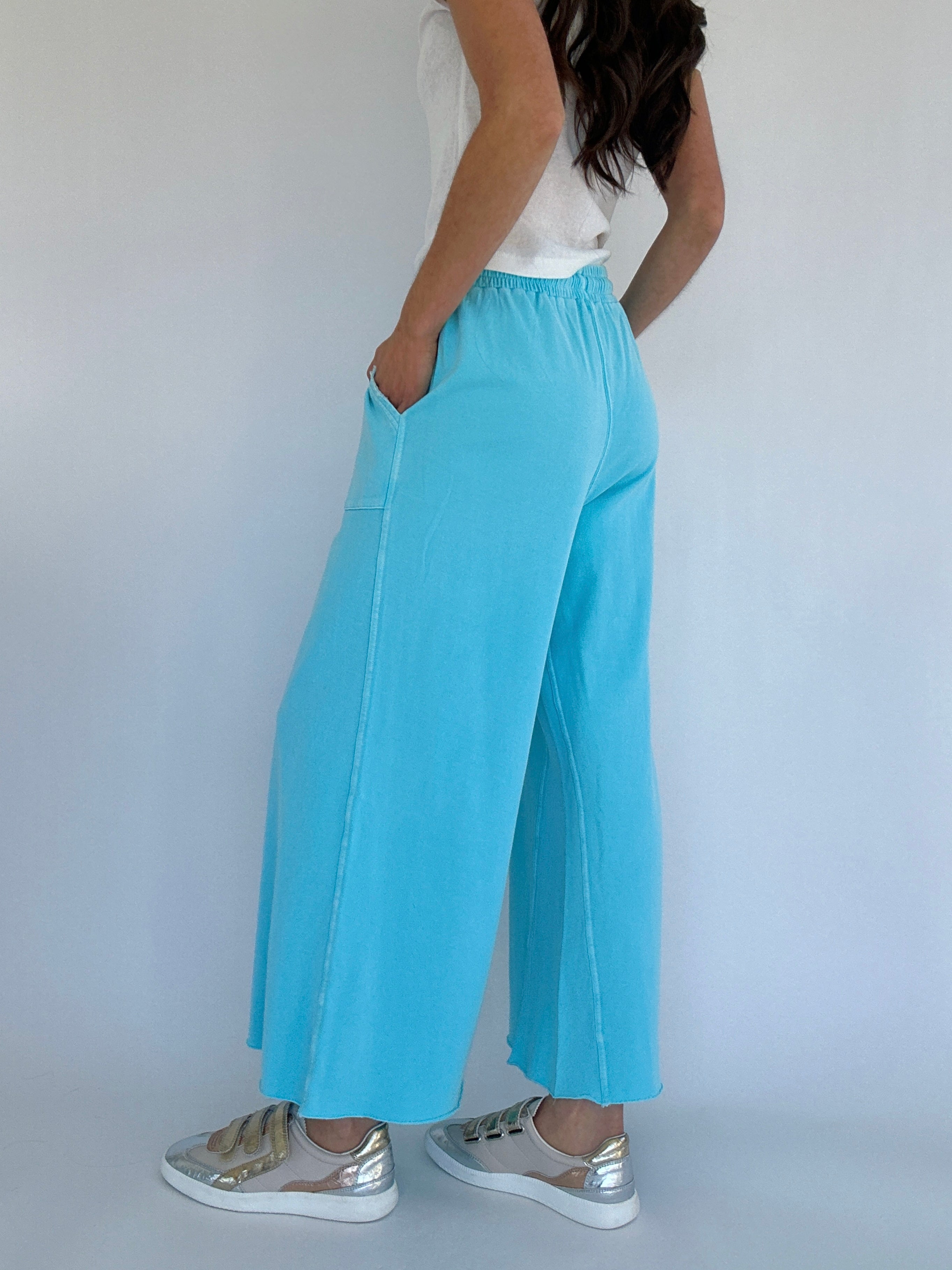 Person wearing light blue wide-leg pants with a white top and silver shoes on a plain background