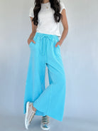 Person wearing light blue wide-leg pants and a white top on a plain background