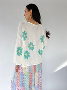 Woman wearing a white blouse with blue floral patterns and a colorful skirt on a plain background