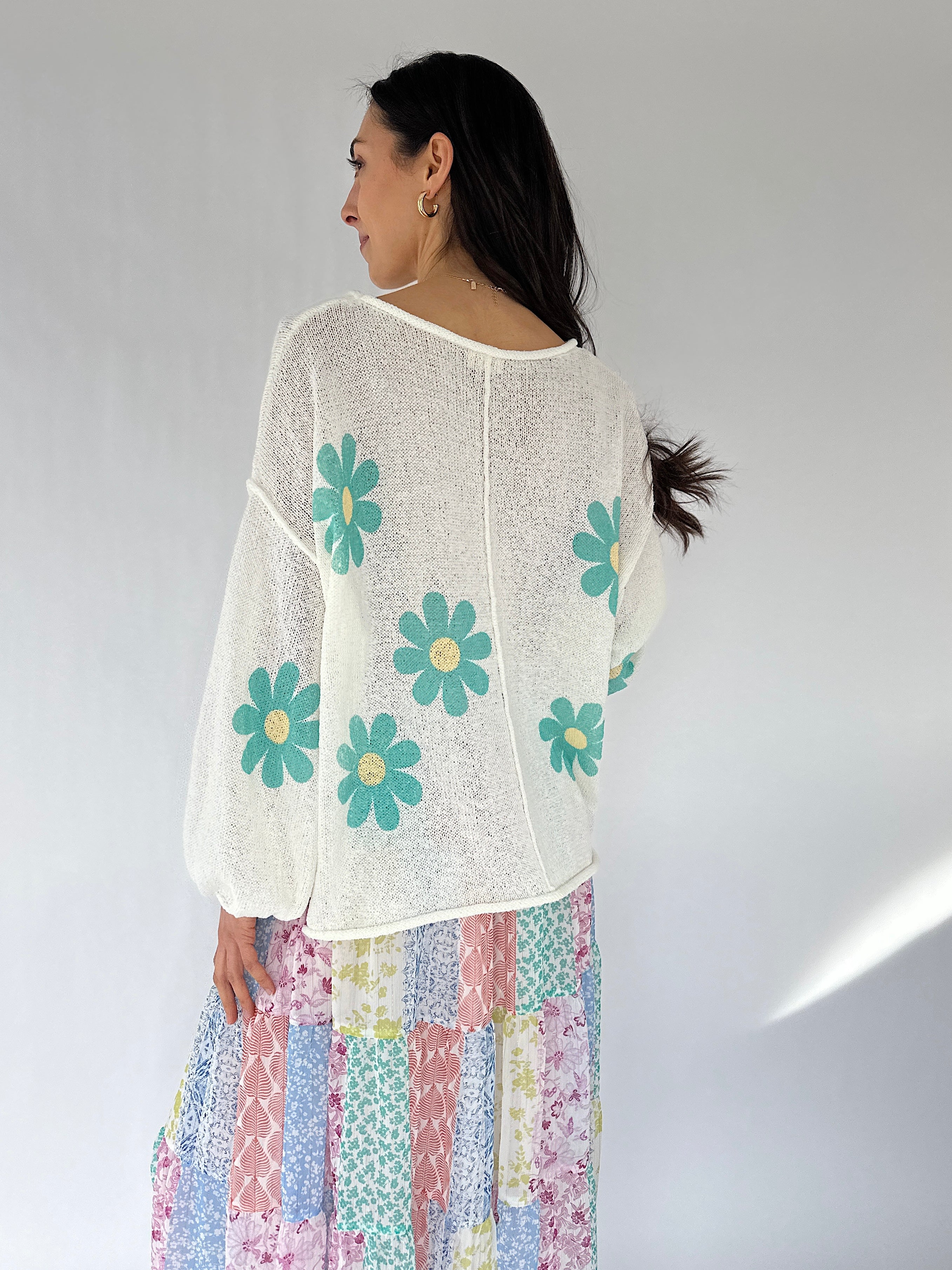 Woman wearing a white blouse with blue floral patterns and a colorful skirt on a plain background