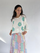 Woman wearing a floral knit top and colorful skirt against a white background