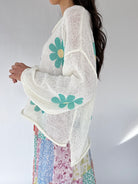 Woman wearing a white knit sweater with floral patterns on a plain background from side