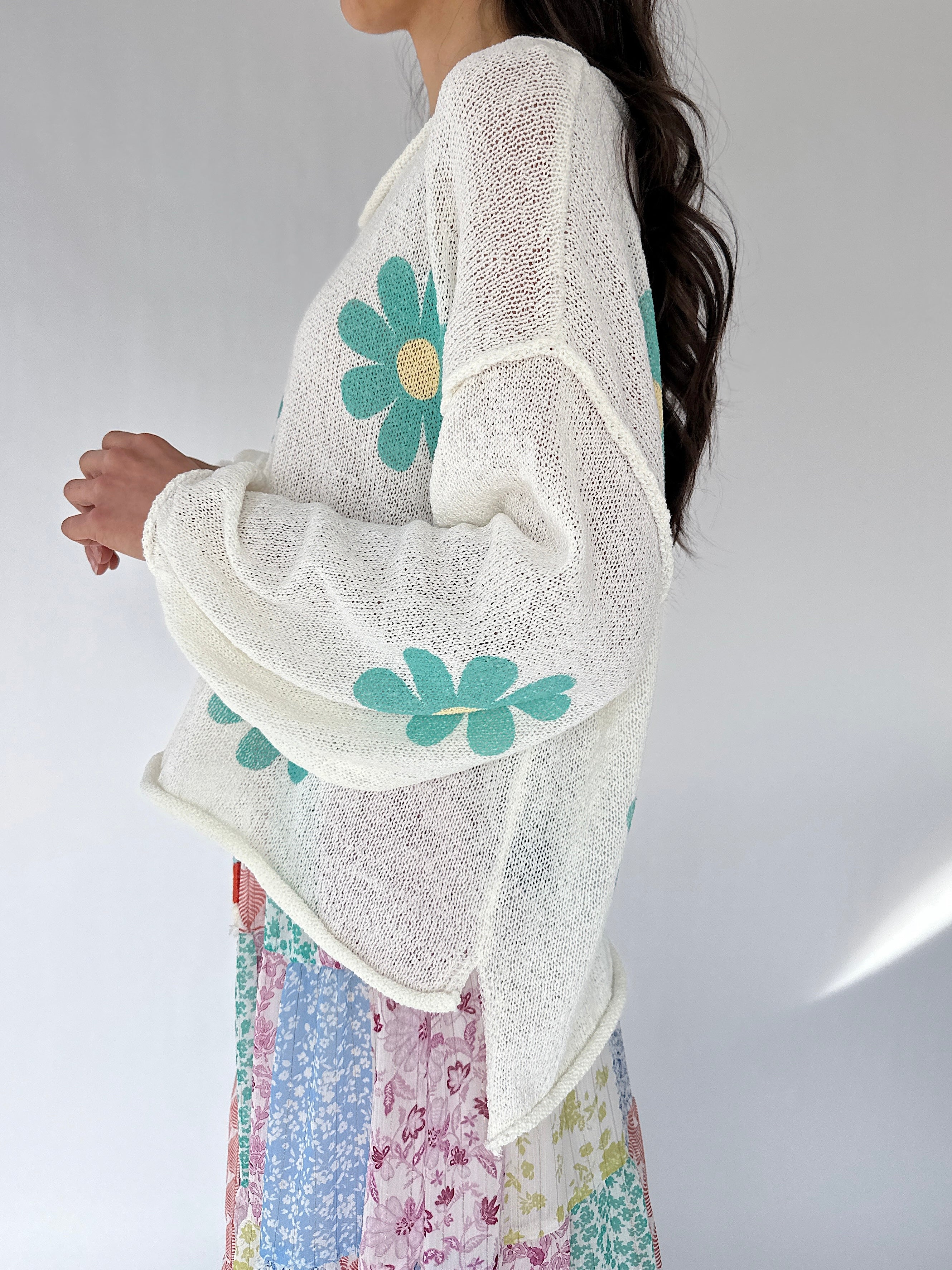Woman wearing a white knit sweater with floral patterns on a plain background from side