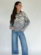 Woman wearing a gray sweater with floral patterns and blue jeans against a white background