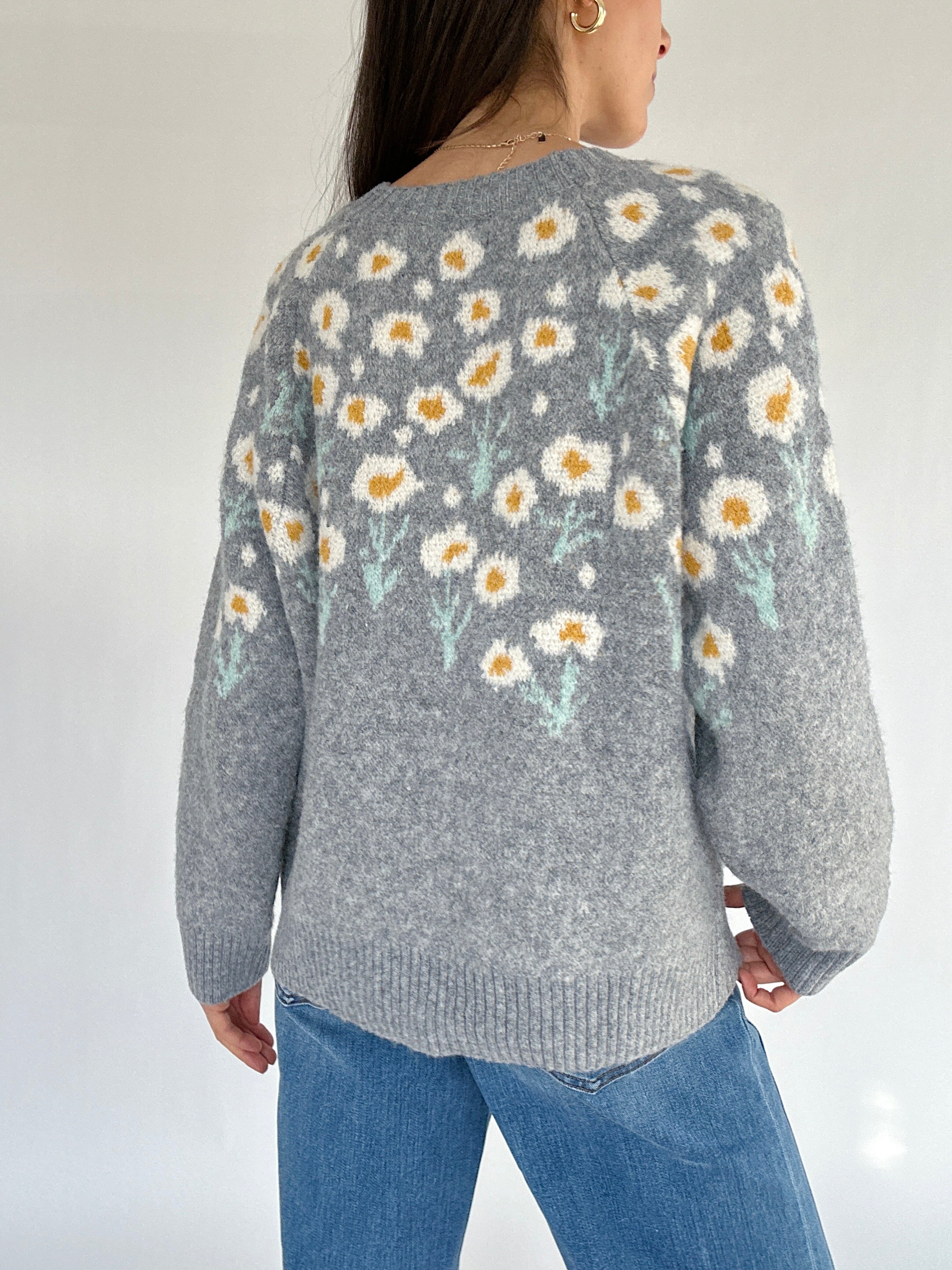 Person wearing a gray sweater with floral pattern on a plain background from the back