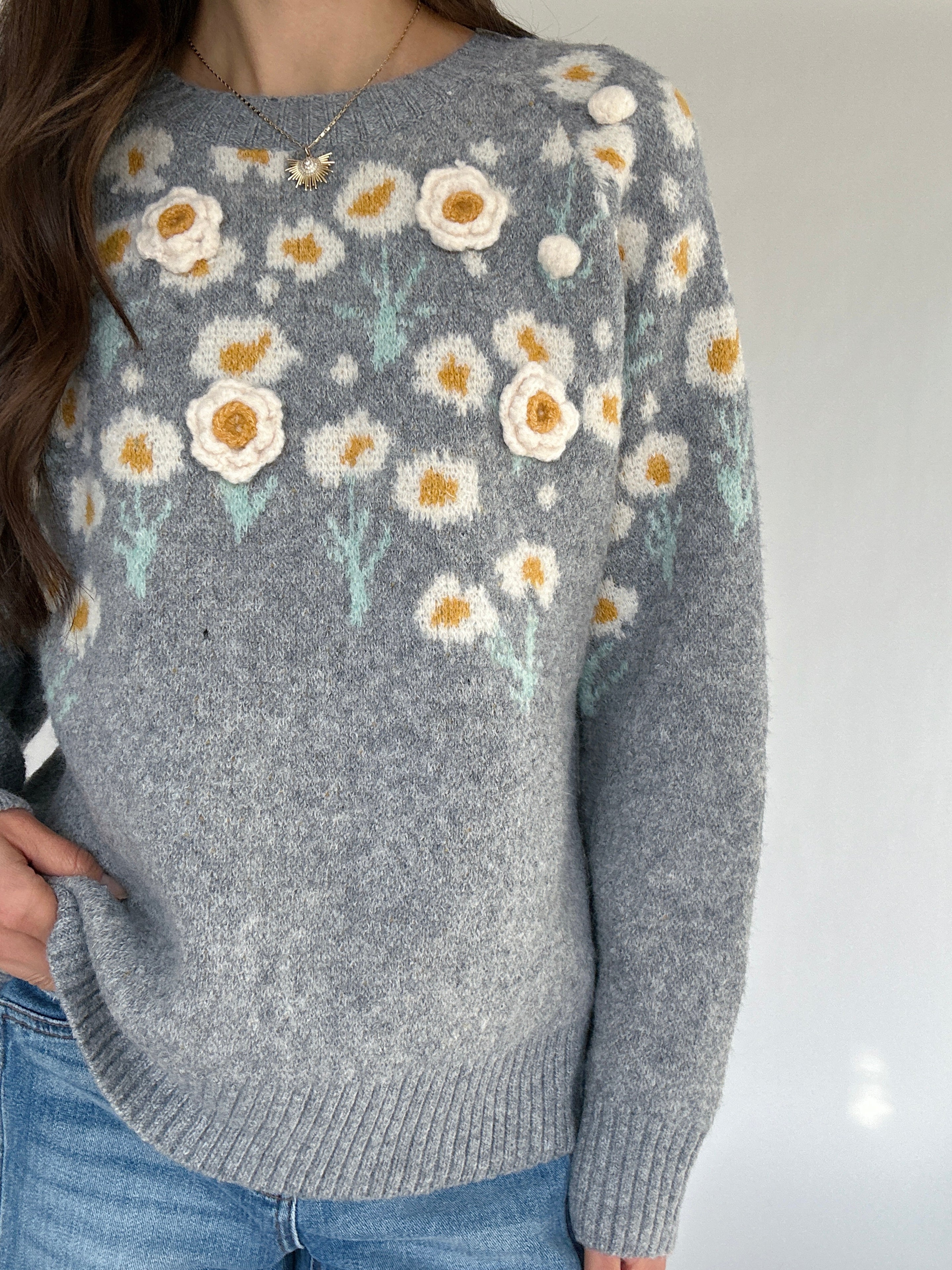Gray sweater with floral patterns worn by a person on a plain background