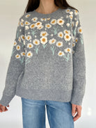Gray sweater with floral pattern worn by a person against a plain background