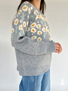 Gray sweater with floral pattern worn by a person on a plain background