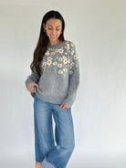Woman wearing a gray sweater with floral patterns and blue jeans against a white background