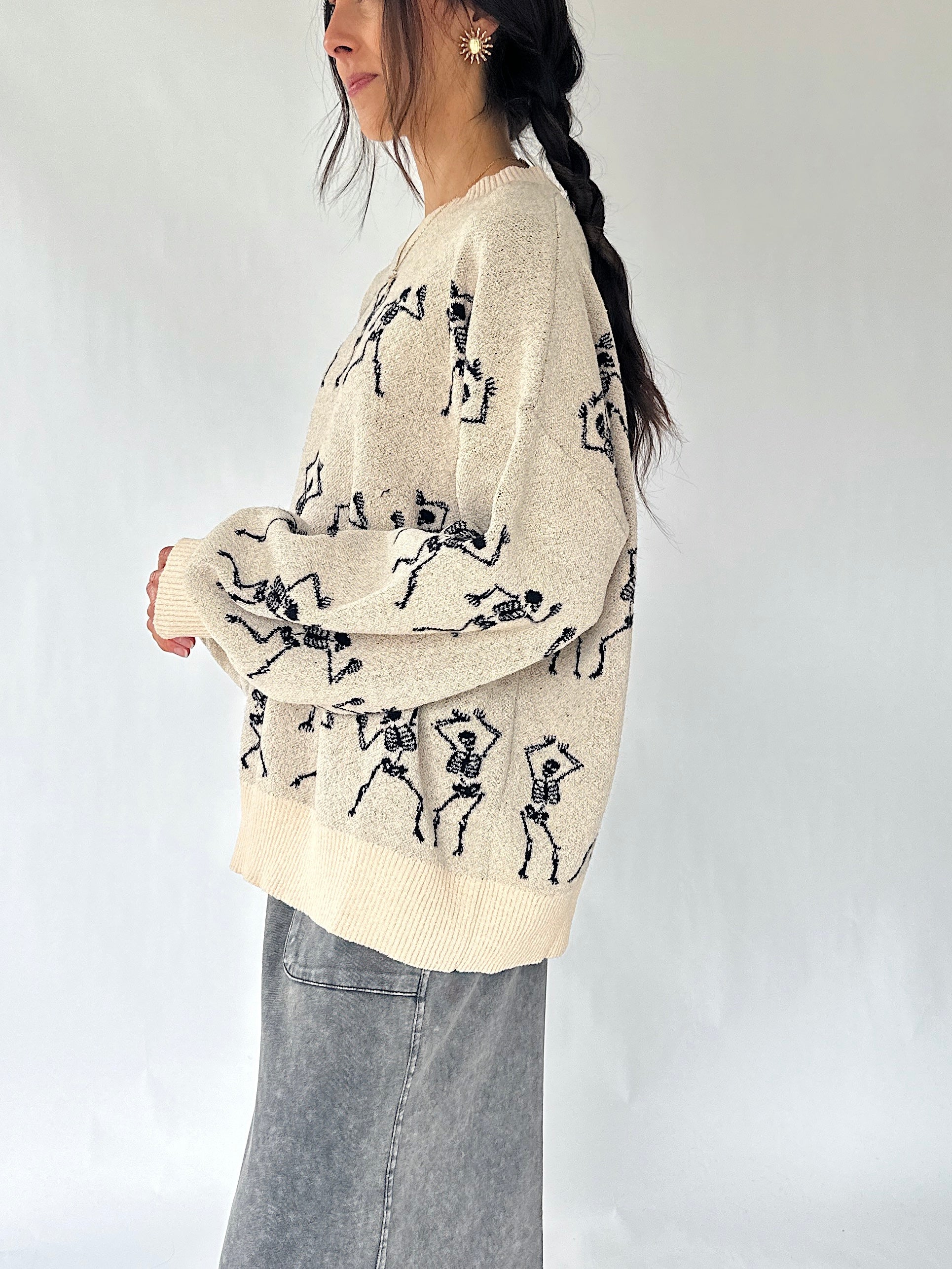 woman standing from the side wearing a cream sweater with dancing skeletons all over