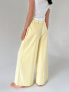 Person wearing light yellow pants and a white top on a plain background
