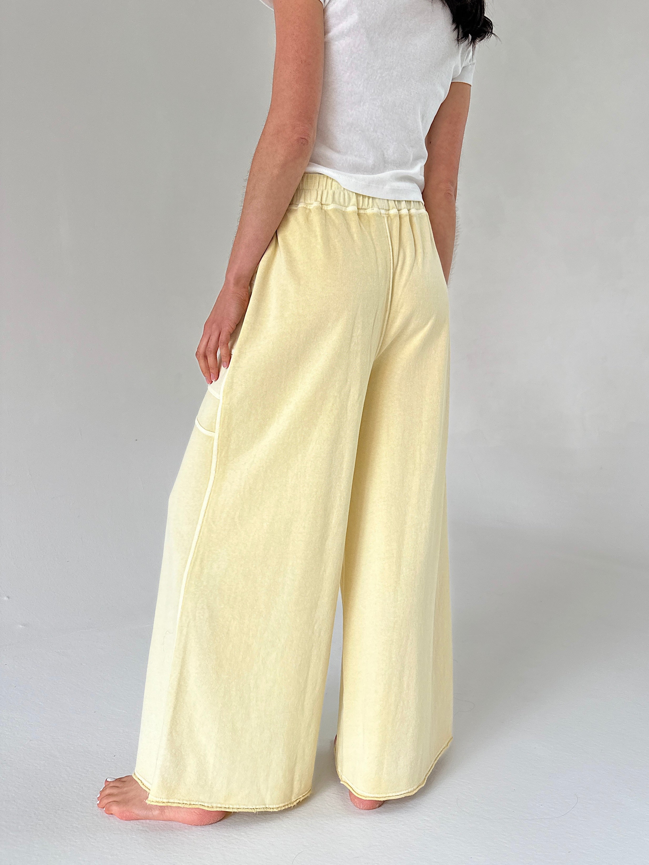 Person wearing light yellow pants and a white top on a plain background