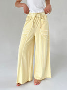 Person wearing light yellow pants with white lines on a plain background