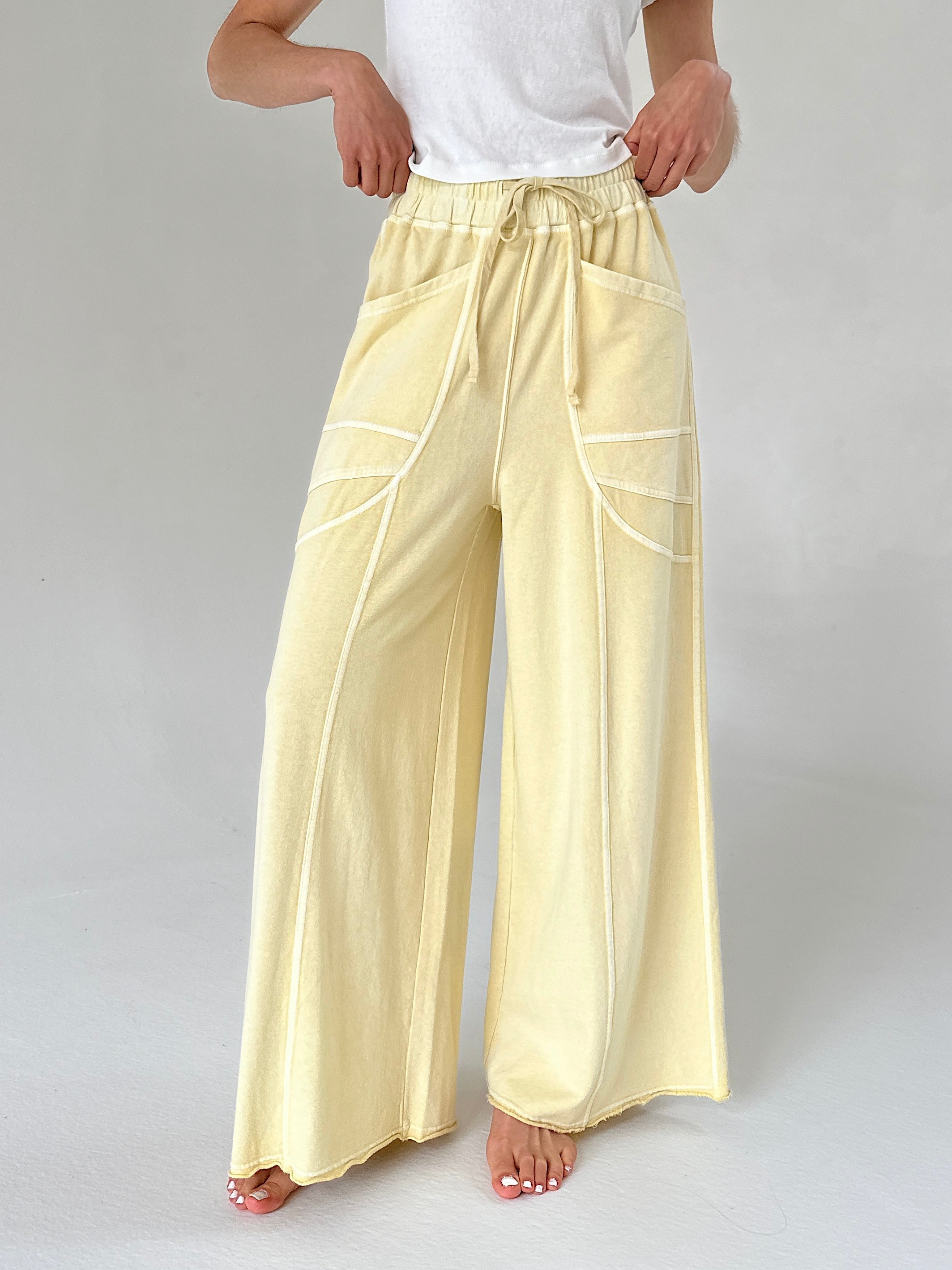 Person wearing light yellow pants with white lines on a plain background