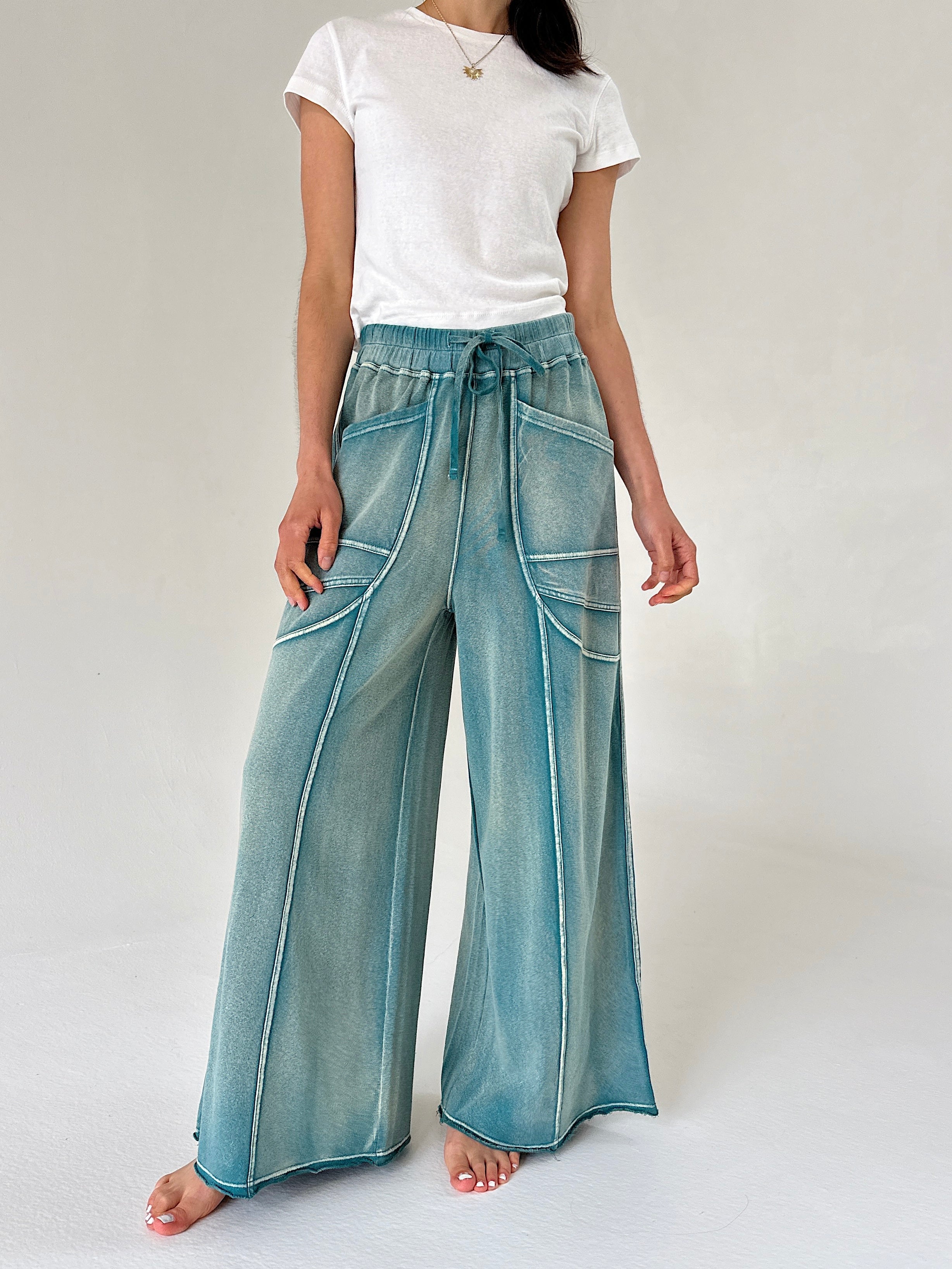 Person wearing teal wide-leg pants and a white t-shirt on a plain background