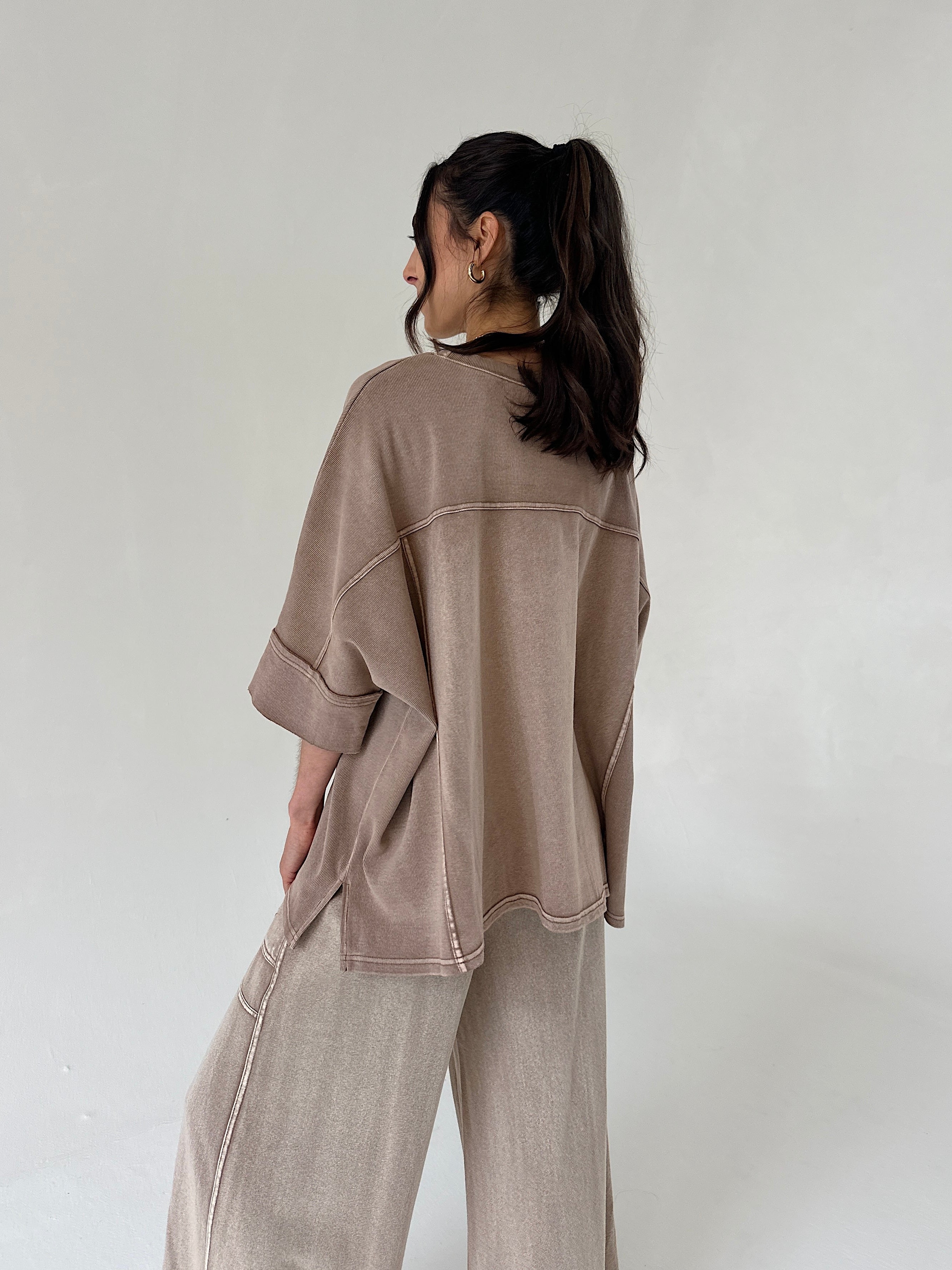 Person wearing a brown top and matching pants against a plain background from back
