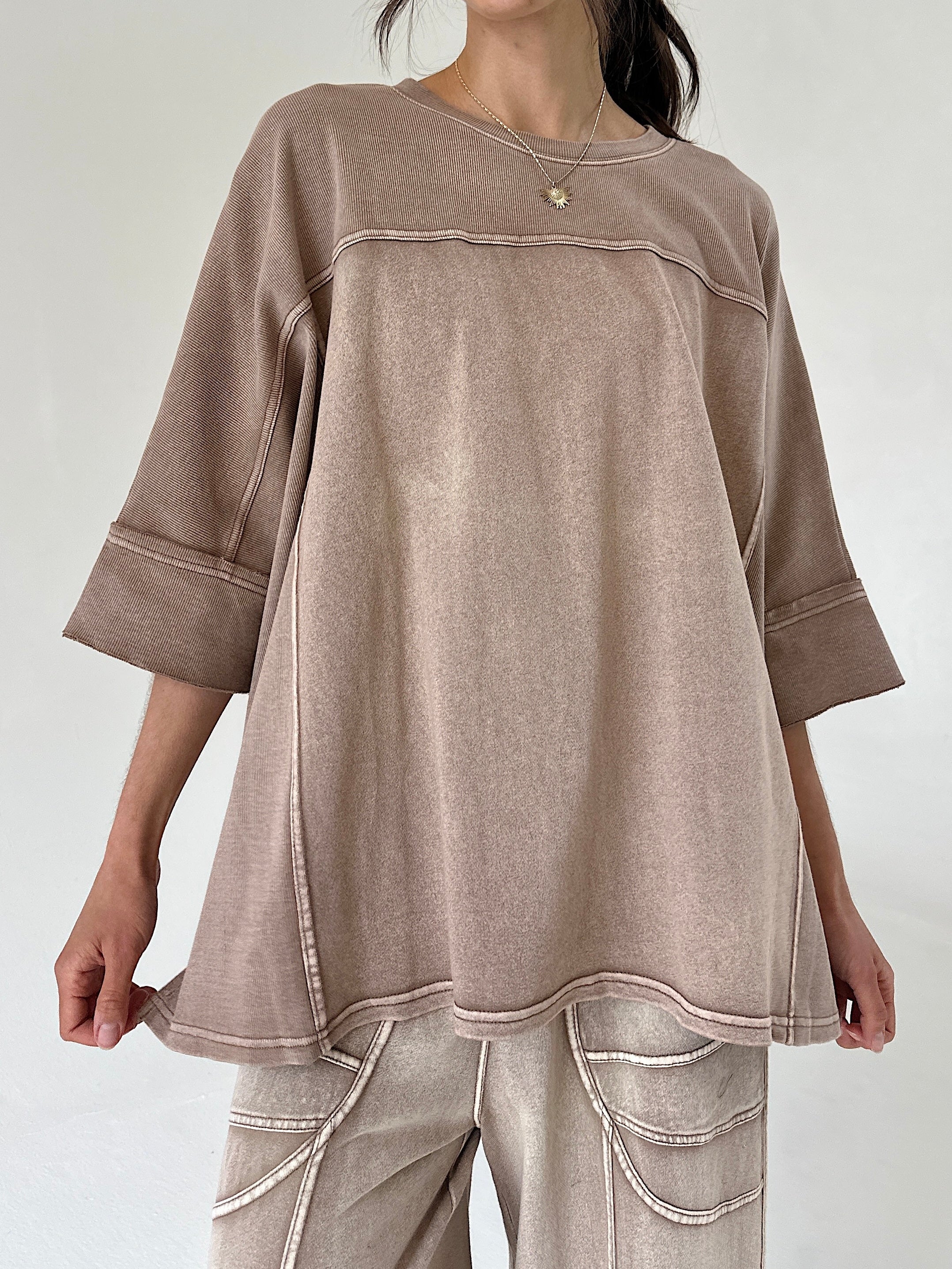 Person wearing a brown oversized top with a plain background