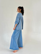 Woman wearing a blue lounge outfit on a plain background from side