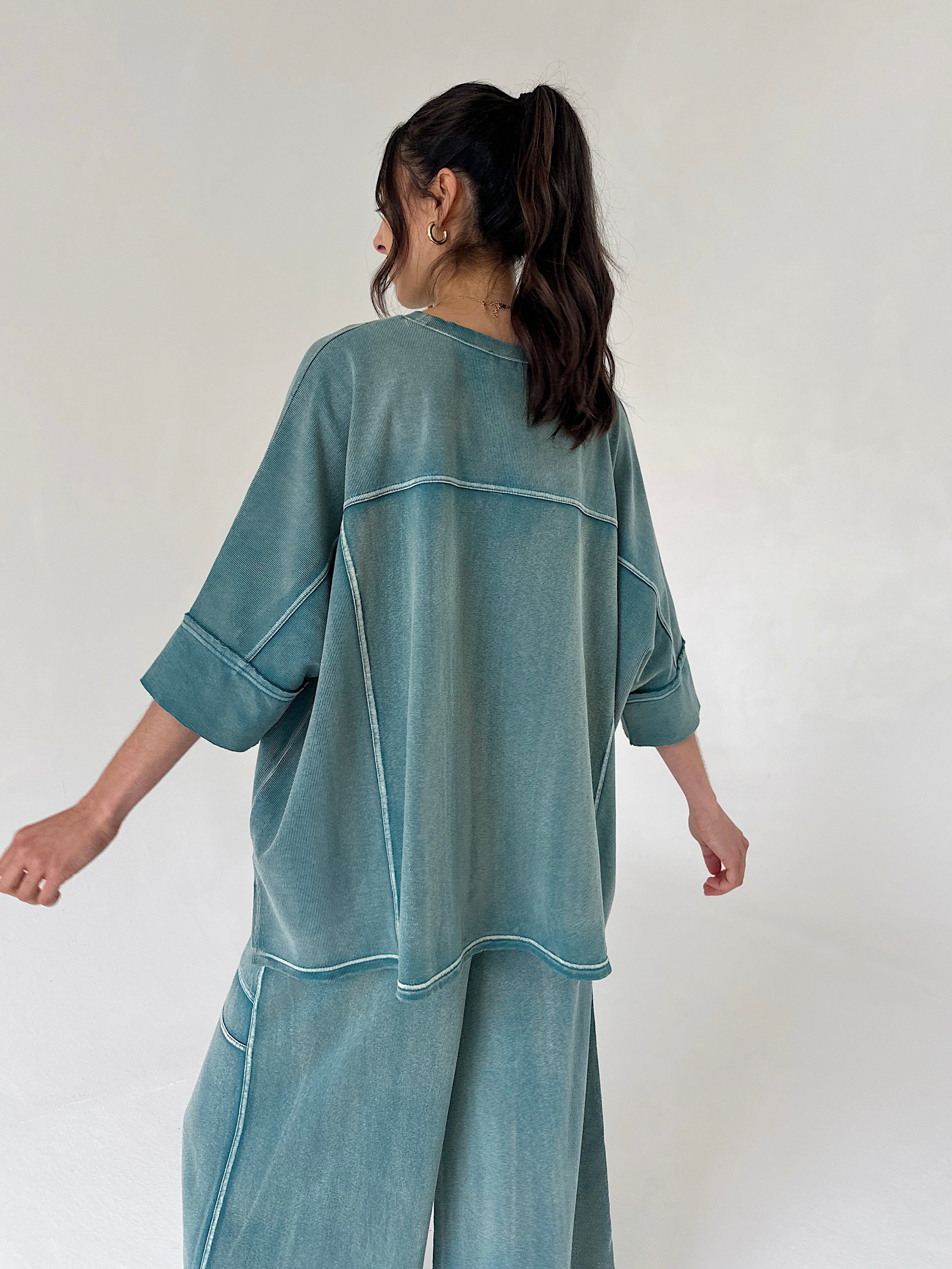 Person wearing a teal oversized shirt and pants set against a white background