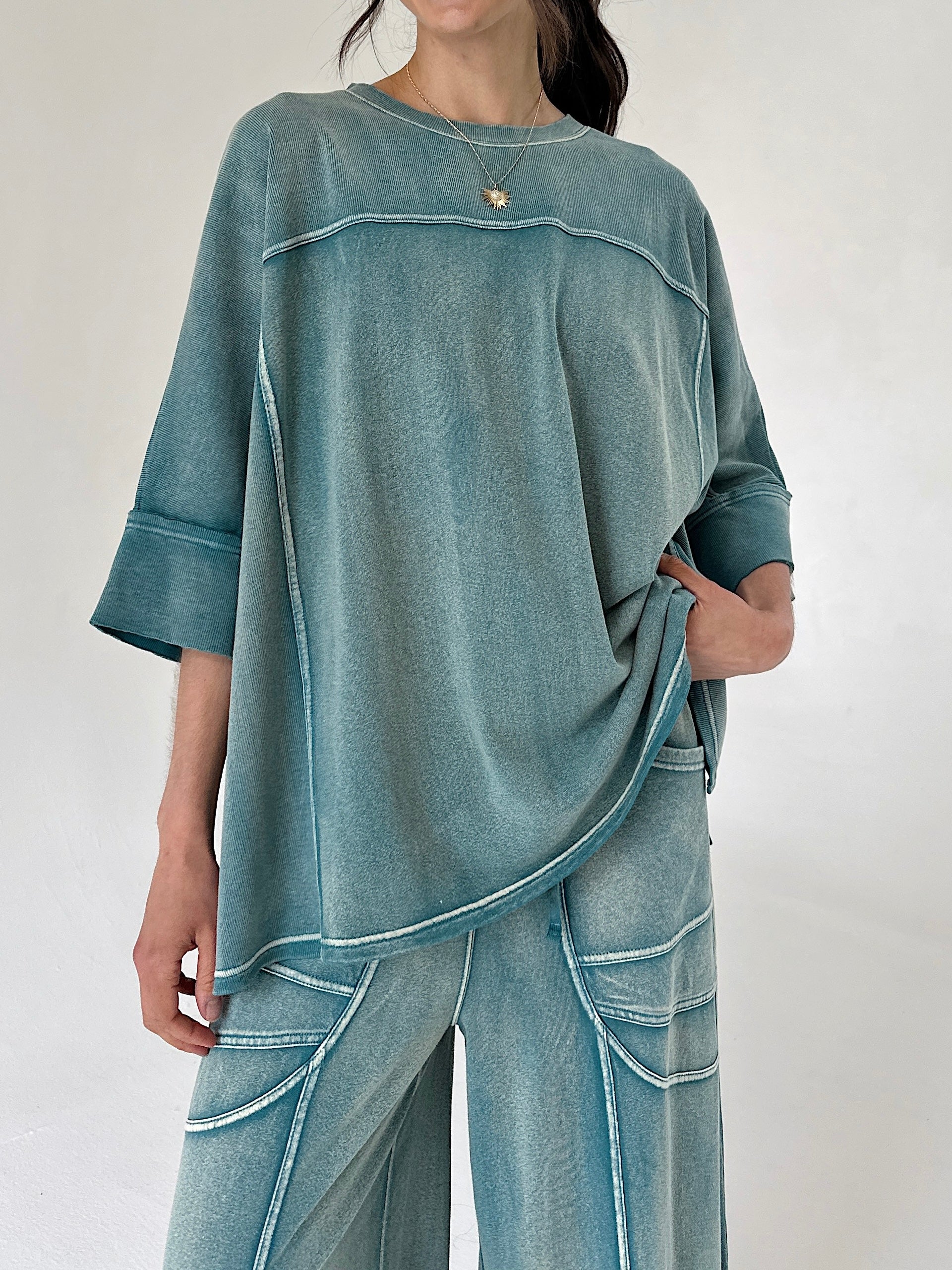 Person wearing a teal oversized top and pants set on a plain background