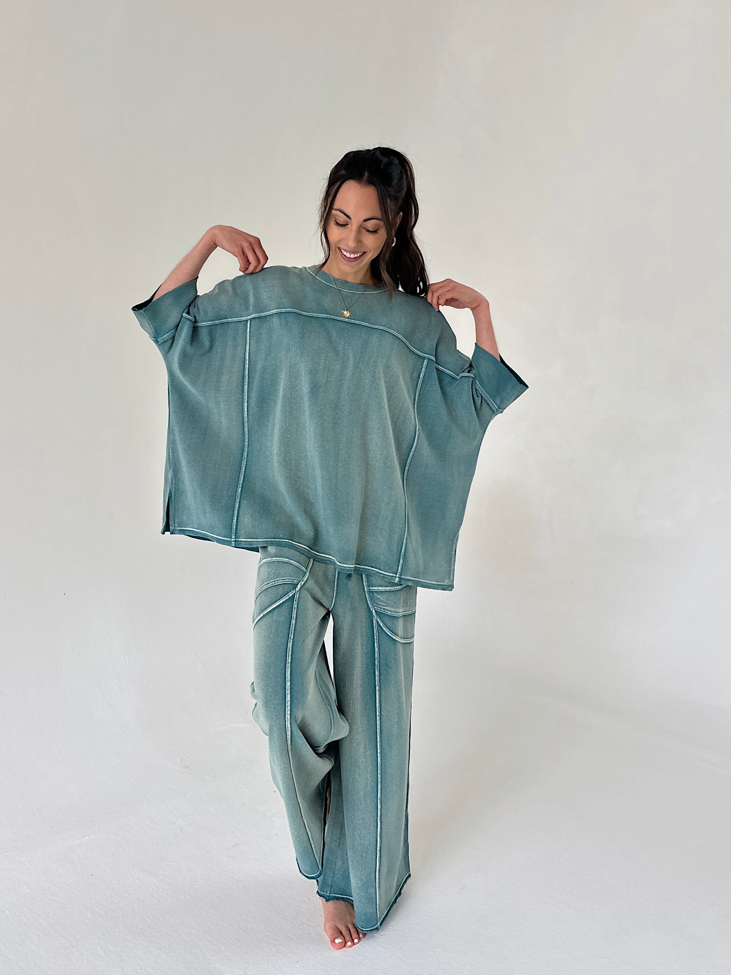 Woman wearing a teal oversized shirt and pants set on a plain background