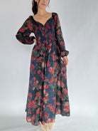 Woman wearing a long floral dress with sweetheart neckline and long sleeves on a plain background
