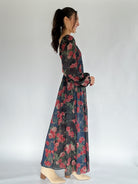 Woman wearing a long floral dress against a white background showing side view